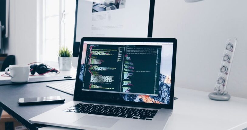 A MacBook with lines of code on its screen on a busy desk